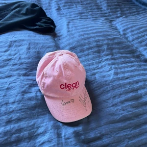 Rosa keps från Clean - Snygg rosa keps från Clean drink som jag vann i en TikTok tävling med broderad logga i rött framtill. Kepsen har justerbar rem baktill för perfekt passform och är signerad av Irma och Marko med hjärtan på skärmen. Perfekt för en avslappnad stil.