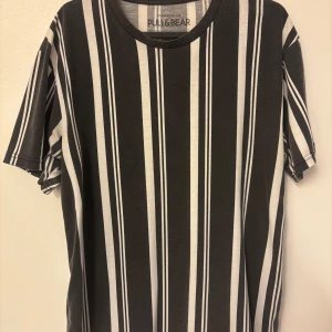Randig t-shirt från Pull&Bear - Svart och vit randig t-shirt från Pull&Bear i storlek M. Klassisk rund halsringning och korta ärmar. Snyggt vertikalt mönster som ger en clean och modern vibe. Perfekt för dig som gillar streetstyle och enkel design.