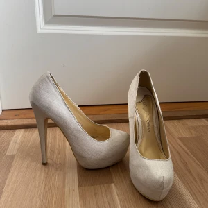 Vita pumps med hög klack - Stilrena pumps i vitt med hög klack och rund tå. Skorna har en elegant satinliknande yta som ger en lyxig känsla. 