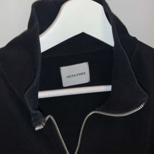 Svart half zip tröja Jack & Jones - Svart långärmad tröja från Jack & Jones med hög krage och silverfärgad half zip-dragkedja. Tröjan har en clean och enkel look, perfekt att styla med jeans eller joggers. Tillverkad i mjuk bomull för skön känsla hela dagen. Pris Kan gå ner i snabbköp