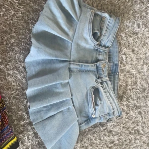 Ljusblå jeanskjol med volang - Superfin ljusblå jeanskjol med bred volang och klassiska jeansdetaljer som fickor och bälteshällor. Kjolen har en kort och utställd modell som ger en cool och trendig vibe. Perfekt för dig som gillar denim och vill sticka ut lite extra. (Sydda med egen hand så det är inte super noggrant gjort) 