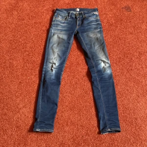 Blå skinny jeans Replay Luz 25 - Snygga blå skinny jeans från Replay, modell Luz. Jeansen har klassisk femficksdesign, slitningar och ljusare partier framtill och baktill. Tydlig Replay-logga vid fickan och bekväm passform med låg midja. Perfekta för en cool och avslappnad stil.