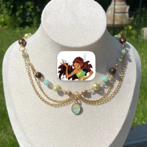 Guldigt halsband med pärlor och kedjor - Unikt halsband med dubbla guldfärgade kedjor och pärlor i brunt, ljusgrönt och blått. Inspirerat från karaktären Layla/Aisha från tv-serien Winxclub. Halsband går att anpassa efter hur man själv vill bära det. Bilderna visar hur det ser ut på mig i två olika längder. 