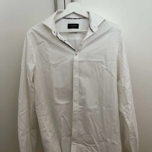 Vit skjorta från Bryan & Sonaglia - Klassisk vit skjorta från Bryan & Sonaglia med lång ärm och knappar framtill. Skjortan har en stilren design med lätt strukturerat tyg och diskreta detaljer vid kragen. Perfekt för dig som gillar en clean och tidlös look.