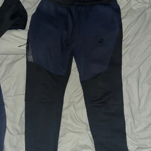 Nike tech fleece  marinblå/svart Sällsynt  - Nike tech fleece set med hoodie och byxor i marinblått och svart. Hoodien har hel dragkedja och stora fickor, byxorna har snörning i midjan och dragkedjeficka. Snygg och sportig look med diskret Nike-logga på både överdel och underdel.