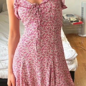 Sommarklänning från Zara  - Supersöt kort blommig klänning från Zara. Klänningen har volangdetaljer vid axlarna, smala axelband och knytning framtill. Lätt och luftig modell, perfekt sommar/midsommar klänning 