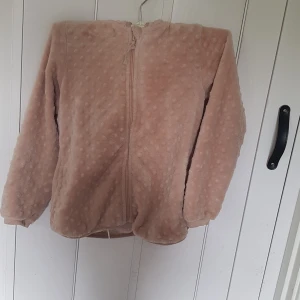 Beige teddyjacka med huva från Pomp de Lux - Supermjuk teddyjacka i beige från Pomp de Lux. Jackan har huva, dragkedja framtill och ett diskret prickigt mönster i tyget. Perfekt för dig som gillar mysiga och stilrena plagg med en chill vibe.