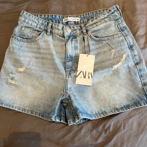 Ljusblå jeansshorts från Zara - Snygga ljusblå jeansshorts från Zara med hög midja och avslappnad passform. Shortsen har slitna detaljer framtill, klassiska fickor och dragkedja med knapp. Perfekta för sommardagar och enkel att matcha med allt. helt nya, aldrig använd! Nypris 329kr