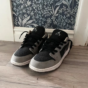 Nike Air Jordan 1 Low grå/svart - Snygga Nike Air Jordan 1 Low sneakers i grått och svart med coola blå detaljer och broderad swoosh. Ovandel i mocka och textil, svart snörning. Priser är inte hugget i sten.