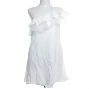 Vit one shoulder klänning Elenza - Superfin vit kortklänning från Elenza med volangdetalj och one shoulder-design. Klänningen har en luftig passform och är perfekt för sommarens varma dagar. Tillverkad i ett lätt material som ger en skön känsla. Köpte denna på sellpy men passade tyvärr inte mig