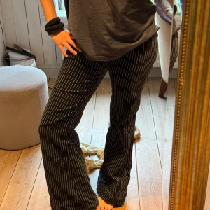 Svarta manchesterbyxor med vita ränder - Säljer ett par svarta manchesterbyxor med smala vita ränder. Byxorna har bootcut-modell och sitter snyggt i midjan. De är i mjuk manchester och har en klassisk pinstripe-look som ger en cool retrovibe. Lite trasiga längst ner på ena benet (se sista bilden)