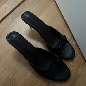 Svarta klackpumps med rosett - Stilrena svarta pumps med öppen tå och smal klack. Skorna har en söt rosettdetalj framtill och är tillverkade i ett slätt material som liknar skinn. Perfekta för dig som gillar en klassisk och chic look. Står 42 på men passar mig som har 40