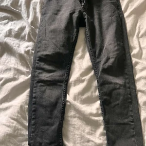  jeans från Nudie Jeans Co - Säljer ett par svarta jeans från Nudie Jeans Co i klassisk slim fit modell. Jeansen har fem fickor, dragkedja och knapp med logga. Materialet är jeans och färgen är mörkgrå/svart, perfekt till en clean och stilren look.