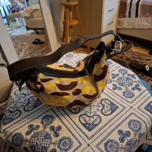 Färgglad axelväska med mönster - Cool axelväska med unikt mönster i gult, brunt och beige. Väskan har breda svarta axelband i skinn och dragkedja upptill. Perfekt storlek för vardagsgrejer och ger en färgklick till din outfit.