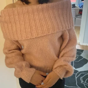 Ljusrosa offshoulder stickad tröja - Supermysig ljusrosa stickad tröja med bred ribbad offshoulder-krage. Tröjan har lång ärm och en loose fit, perfekt för dig som gillar en chill och trendig look. Passar grymt till både jeans och kjol.