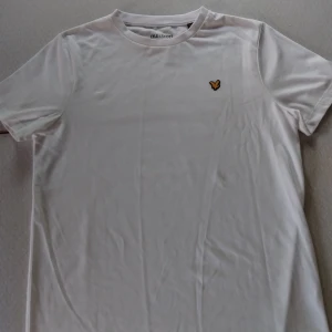 Vit t-shirt från Lyle & Scott - Vit t-shirt från Lyle & Scott med klassisk rund hals och korta ärmar. På bröstet sitter den ikoniska gula örnloggan. T-shirten är i mjuk bomull och har en clean, stilren look som passar perfekt till jeans eller shorts. Nypris 300kr fast säljer för 120kr
