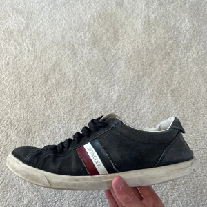 Skor från moncler - Säljer ett par svarta Moncler sneakers med klassiska rödvita ränder på sidan och Moncler-logga. Skorna har snörning, vit sula och rund tå. Perfekta för dig som gillar stilrena skor med premiumkänsla. Skorna passar en med storlek 44-44,5. Priset kan diskuteras. Vid frågor är det bara skriva!