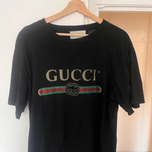 Svart Gucci t-shirt med broderad blomma - Svart t-shirt från Gucci med klassisk logga! Även en blomma i nacken samt så är den distressed i kragen! Passar L/XL