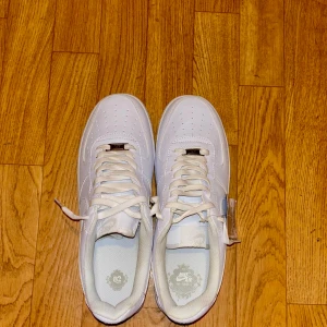 Nike Air Force 1 vita  - Klassiska Nike Air Force 1 sneakers i helvitt skinn med lågt skaft och rund tå. Snygg och clean design med perforerade detaljer på tån och ikoniska swoosh-loggan på sidorna. Perfekta för dig som gillar streetstyle och vill ha en tidlös look. Finns både storlek 45 och 42.