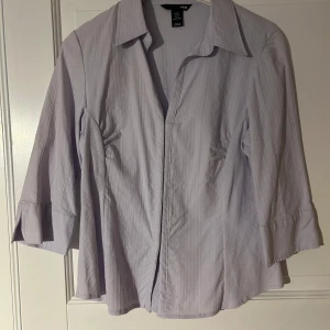 Ljuslila randig skjorta från H&M - Snygg ljuslila skjorta från H&M med diskreta ränder och klassisk krage. Skjortan har trekvartsärmar och är tillverkad i ett lätt bomullstyg. Perfekt för dig som gillar en stilren och enkel look.