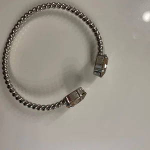 Silverfärgat armband Caroline Svedbom - Snyggt armband från Caroline Svedbom i silverfärgad metall med tvinnad design. Armbandet är öppet och har två stora, ljusgula kristaller i varje ände som ger en lyxig känsla. Perfekt statement piece för att lyfta din outfit.