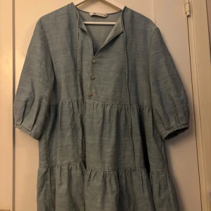Blå loose klänning från Zara - Supersöt ljusblå klänning från Zara med volanger och trekvartsärm. Klänningen har dekorativa pärlknappar framtill och en avslappnad, loose passform. Perfekt för vår och sommar, och lätt att styla med sneakers eller boots. passar även s