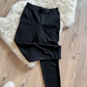 Svarta kostymbyxor med resår - Svarta kostymbyxor med elastisk midja bak och klassiska fickor fram. Byxorna har raka ben och är sydda i ett mjukt tyg som känns bekvämt hela dagen. Perfekta för en clean och stilren look.