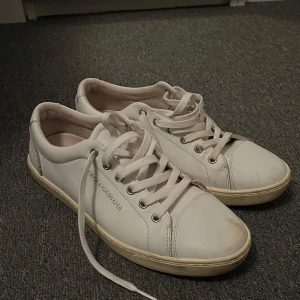 Vita sneakers från Dolce & Gabbana - Stilrena vita sneakers från Dolce & Gabbana i skinn med klassisk låg profil och rund tå. Skorna har vita snören, silverfärgade öljetter och diskret logga på sidan. Perfekta för dig som gillar minimalistisk och clean look. Ingen box till eftersom det var en gåva från en släkting. Använda men syns knappast.