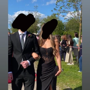 Svart axelbandslös långklänning med spets - Supersnygg svart långklänning med axelbandslös korsettdesign, glittrande spetsdetaljer och snörning i ryggen. Klänningen har figurnära passform, slits framtill och transparent mesh upptill. Perfekt för bal eller festkvällar när du vill sticka ut. Köpt från ZAPAKA, betalade ca 1600kr. Kvitto finns.