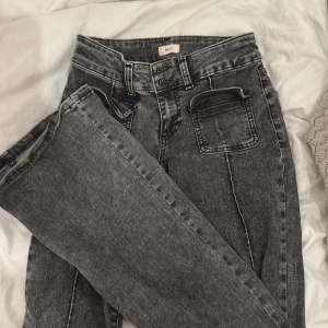 Gråa bootcut jeans från Nelly - Snygga gråa bootcut jeans från Nelly med låg midja och markerade sömmar längs benen. Jeansen har två framfickor och bälteshällor, tillverkade i stretchig denim för en bekväm passform.