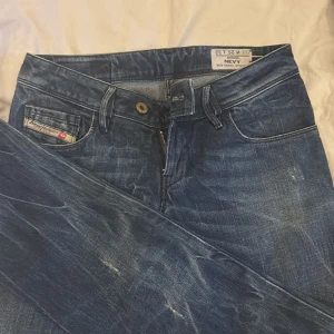 Blå Diesel jeans med slitningar - Säljer ett par blå jeans från Diesel med snygga slitningar och tvättade detaljer. Klassisk femficksmodell med Diesel-logga på fickan och svart patch bak i midjan. Jeansen har rak passform och normal midja, perfekta till sneakers eller boots.