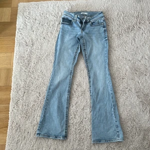 Ljusblå bootcut jeans med fickdetaljer - Snygga ljusblå jeans med bootcut passform och klassiska fem fickor. Baksidan har fickor med lock och knappdetaljer. Jeansen har normal midja och är tillverkade i mjukt denimtyg. Perfekta för en avslappnad och trendig look.