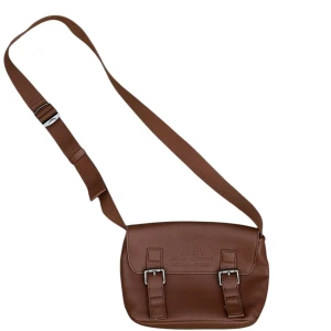 Brun axelväska från Zara i skinn - Snygg brun axelväska från Zara i skinn med justerbar rem och två spännen framtill. Väskan har magnetlås, innerfack med dragkedja och stilren design. Perfekt för dig som vill ha en praktisk och trendig väska med plats för det viktigaste.