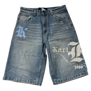 Karl Kani baggy jorts med tryck - Riktigt feta blå jeansshorts från Karl Kani med stora tryck och broderier både fram och bak. Baggy passform, klassisk femficksdesign och coola detaljer som texten 'Karl Kani 1989' och broderad bakficka. Perfekta för dig som gillar streetwear och old school vibes.