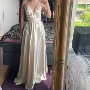 Champagnefärgad långklänning/balklänning - Elegant långklänning i skimrande champagnefärgad satin med djup v-ringning och tunna axelband som korsas i ryggen.Klänningen har markerad midja och ett vackert fall.Perfekt för bal eller student!Klänningen är från butiken ivoryfield i sthlm.Klänningen säljs för 2499kr och jag säljer den för att min rätt till retur har gått ut och behöver få klänningen såld.Aldrig använd,en sprillans ny nyhet och så fin.Storlek 34/2men passar mig som bär storlek S.Kontakta för fler bilder,vinklar &mer information