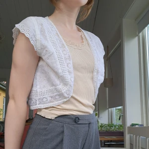 Vit spetsväst från Lindex - Söt vit väst från Lindex i bomull med broderade blommor och spetsdetaljer. Kort modell med volangkantade ärmhål och öppen front. Perfekt att slänga över ett linne för en romantisk vibe. Har gula fläckar, se sista bilderna, men det märks knappt när man har på sig den. 