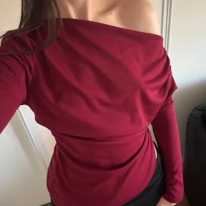 Vinröd offshoulder topp med drapering - Säljer en vinröd långärmad topp med snygg offshoulder-design och draperad effekt över bröstet. Aldrig använd! 