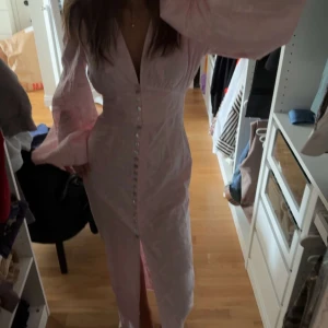 Ljusrosa Adoore - Säljer min helt oanvända Adoore klänning i storlek 34, superfin ljusrosa långklänning med djup v-ringning, markerad midja och stora puffärmar. Klänningen har knappar framtill hela vägen ner och en slits som ger en snygg siluett. Materialet är lätt och har en subtil struktur som känns lyxig.  Prislapp kvar