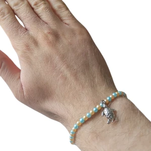 Pärlarmband med sköldpaddshänge - Armband med små pärlor i turkos och guld, dekorerat med ett silverfärgat sköldpaddshänge. 
