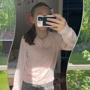 Ljusrosa kofta från Divided - Söt ljusrosa kofta från Divided med rund halsringning och knappar framtill. Långärmad och i mjukt, tunt material som passar perfekt till lager-på-lager. Enkel och stilren design som är lätt att matcha.