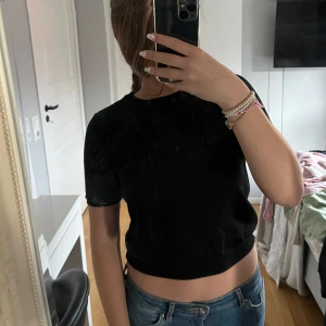 Svart croppad topp från H&M - En svart croppad topp från H&M med korta ärmar och rund hals. Enkel och stilren design som passar perfekt till jeans eller kjol. Mjuk och bekväm, tillverkad i ett stretchigt material som sitter snyggt på kroppen.