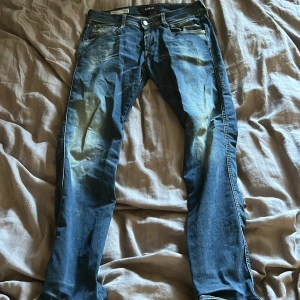 Replay Anbass blå jeans herr - Snygga blå Replay Anbass jeans med klassisk femficksdesign och slitna detaljer framtill. Jeansen har smal passform och är tillverkade i mjukt denimtyg med stretch för extra komfort. Perfekta för en avslappnad och trendig look.