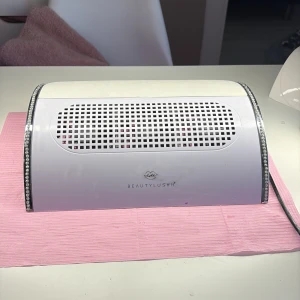 BeautyLush nageldammsugare/utsug med strass - Nageldammsugare från BeautyLush i vit plast med glittriga strassdetaljer längs kanterna. Utrustad med av/på-knapp och tillhörande dammpåse. Perfekt för att hålla nagelbordet rent vid manikyr och nagelfix.