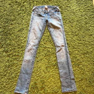 True Religion ljusblå jeans, stl 24 - Säljer ett par ikoniska ljusblå jeans från True Religion med klassiska kontrastsömmar och snygga detaljer på bakfickorna. Modellen har låg midja och raka ben, tillverkade i mjukt jeanstyg. Perfekta för dig som gillar en tidlös och cool denimlook.