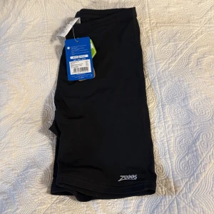 Svarta badshorts Zoggs Ecolast+ - Svarta, tighta badshorts från Zoggs i modellen Cottesloe Mid Jammer. Tillverkade i Ecolast+ material som är snabbtorkande och stretchigt. Helt nya Aldrig använda🤩🧞‍♂️