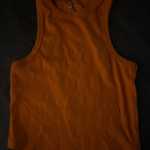 Ribbad orange linnetopp - Säljer en ribbad orange linnetopp i stretchigt material. Perfekt för varma dagar och enkel att matcha med jeans eller shorts. Modellen är ärmlös och har rund halsringning.