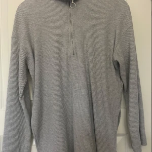 Ljusgrå ribbad polotröja med dragkedja - Säljer en ljusgrå ribbad polotröja med halv dragkedja. Tröjan har lång ärm och är lite längre i modellen . Enkel och stilren design som passar till det mesta.