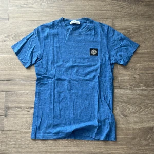 Blå t-shirt från Stone Island - Säljer en blå t-shirt från Stone Island med klassisk logotyp-patch på bröstet. T-shirten har rund hals och är tillverkad i mjuk bomull. Använd ett par gånger men fortfarande bra skick, pris kan diskuteras vid snabb affär, storleken passar xs bra