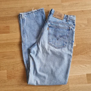 Ljusblå Levis 550 relaxed fit jeans - Klassiska ljusblå Levis 550 jeans med raka ben och hög midja. Jeansen har fem fickor, knappgylf och en liten slitning på ena knät för en cool vintagekänsla. Lite slitage mellan benen men inget son stör/syns. Ca 73 cm i midjemått.