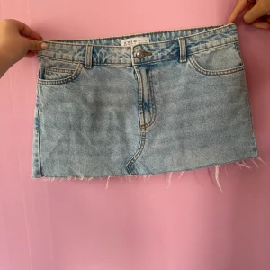 Ljusblå jeanskjol med rå kant - Säljer en ljusblå jeanskjol med klassiska fickor fram och bak samt bälteshällor. Kjolen har en rå, fransig kant nedtill för en cool och avslappnad look. Perfekt att styla med sneakers eller boots. Modellen är lite kortare!
